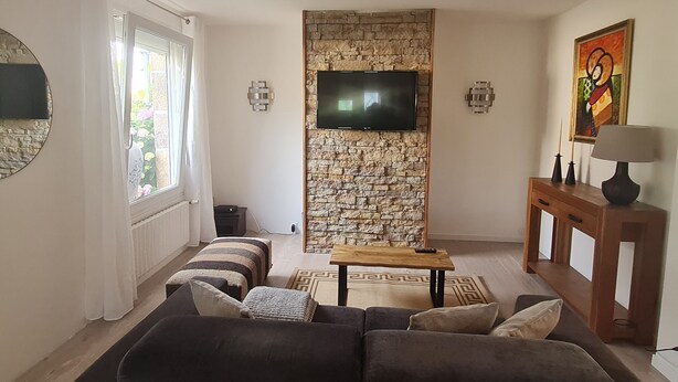 Uma sala de estar com parede de pedra, TV de tela plana, sofá, mesa de centro e luminária.