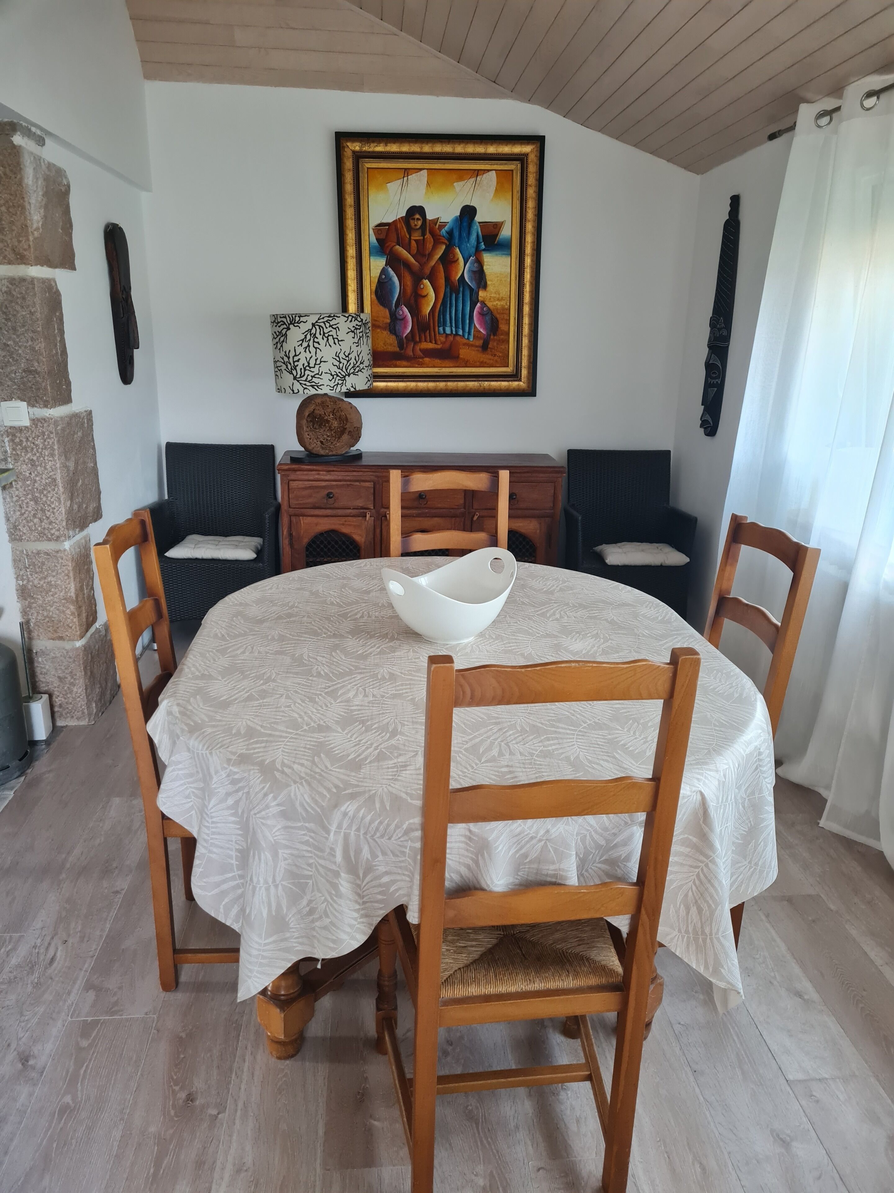 Un comedor con una mesa redonda, sillas de madera, mantel blanco, un cuadro en la pared y una pared de piedra.
