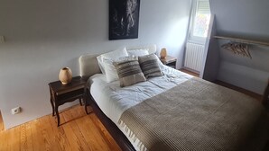 Quarto com cama, mesas de cabeceira, obra de arte na parede, janela com persianas e radiador.