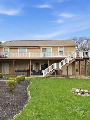 A two-story house with a covered porch, a staircase, and a well-maintained lawn. - Enjoy this fully functional guest house with a beautiful backyard and forest! (Powell)