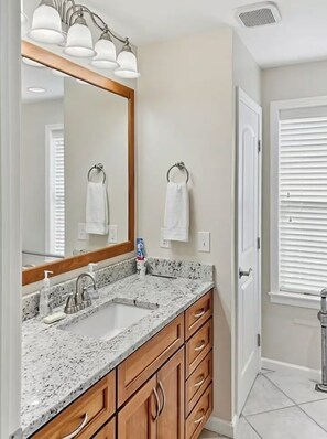 A bathroom with a granite countertop, wooden cabinetry, a large mirror, and a towel rack. - Enjoy this fully functional guest house with a beautiful backyard and forest! (Powell)