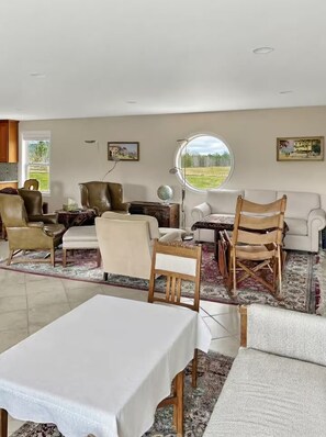 A living room with a dining table, chairs, sofas, a coffee table, and a large window with a view of a field. - Enjoy this fully functional guest house with a beautiful backyard and forest! (Powell)