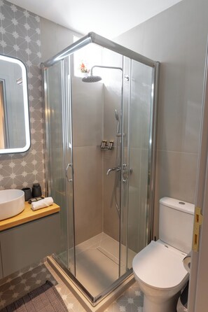 A modern bathroom with a glass-enclosed shower, a toilet, and a sink with a mirror above it. - Ground Living - Apartment Two (Volos)
