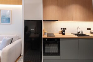 A modern kitchen with a built-in oven, a black refrigerator, and wooden cabinets. - Ground Living - Apartment Two (Volos)