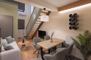 Una sala de estar moderna con una escalera, una mesa de comedor con sillas, un sofá y una planta en maceta.