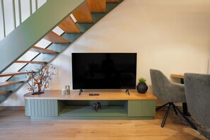 Una sala de estar con televisor de pantalla plana, una escalera, una planta y un sillón.