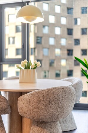 A modern dining area with a round table, two textured chairs, a pendant light, and a vase with white flowers. - Cozy City Stay | Free Parking (Montréal)