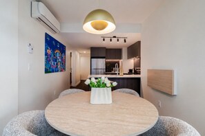 A modern dining area with a round table, white vase with flowers, and a pendant light. - Cozy City Stay | Free Parking (Montréal)