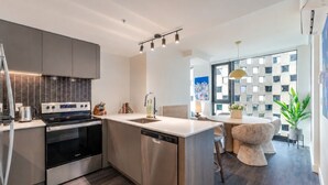 A modern kitchen with stainless steel appliances, a central island, and a dining area with a round table and chairs. - Cozy City Stay | Free Parking (Montréal)