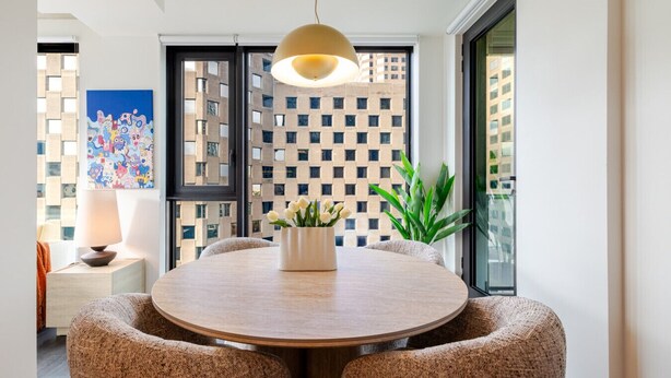 A dining area with a round table, two chairs, a pendant light, a potted plant, and a colorful abstract painting on the wall. - Cozy City Stay | Free Parking (Montréal)