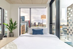 A modern hotel room with a large bed, a city view, and a potted plant. - Cozy City Stay | Free Parking (Montréal)