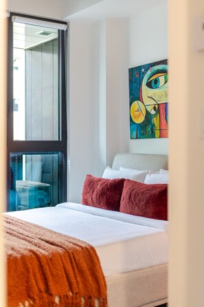 Een hotelkamer met een bed, een raam met zonwering, een schilderij aan de muur en uitzicht op buiten.