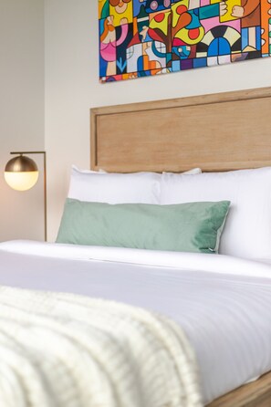 Ein Bett mit weißen Leinentüchern, einem grünen Kopfkissen und einem hölzernen Kopfteil.