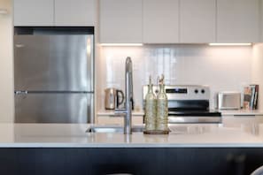 A modern kitchen with stainless steel appliances, a central island with a sink, and two decorative glass bottles. - Modern Downtown Stay | Pool & Skyline (Montreal)