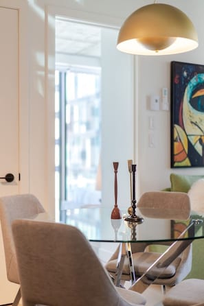 A modern living room with a glass coffee table, two chairs, a brass lamp, and a colorful abstract painting on the wall. - Modern Downtown Stay | Pool & Skyline (Montreal)