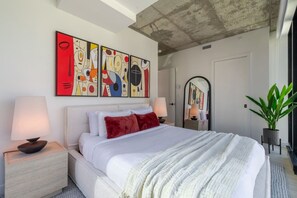 A modern bedroom with a large bed, two bedside tables with lamps, a mirror, and abstract artwork on the wall. - Modern Downtown Stay | Pool & Skyline (Montreal)