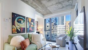 A modern living room with a green sofa, a glass coffee table, and abstract art on the wall. - Modern Downtown Stay | Pool & Skyline (Montreal)
