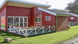 A red building with a covered porch and a fenced outdoor area. - 6 Person Holiday Park Home in Gudhjem (Gudhjem)
