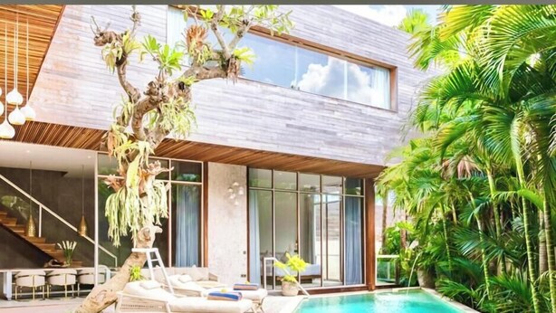 Ein modernes Haus mit Schwimmbad, Liegestühlen und tropischen Pflanzen.