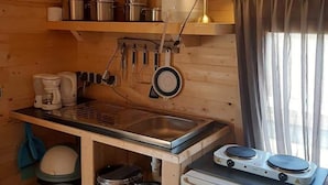 Una cocina compacta con paredes de madera, un lavamanos de acero inoxidable, un refrigerador pequeño y electrodomésticos básicos.