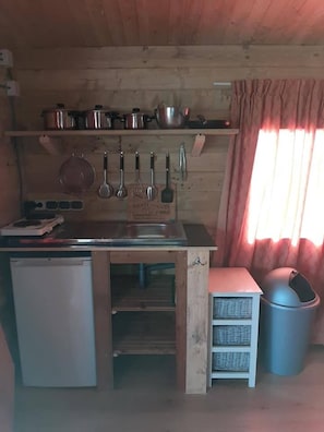 A compact kitchen with wooden walls, a sink, a small refrigerator, a stove, and a trash bin. - Cabin Sleeps 4 With Hot Tub and Garden (Hitzum)