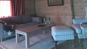 Interior de una cabaña de madera con sofá, mesa de centro, sillón y un cuadro en la pared.