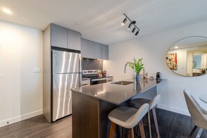 A modern kitchen with a stainless steel refrigerator, a built-in oven, and a large island with bar stools. - Stylish Downtown Retreat | Pool & Views (Montreal)