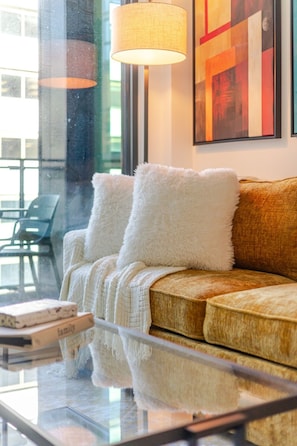 Uma sala de estar moderna com um sofá, almofadas brancas e fofas, uma mesa de centro de vidro e uma luminária.