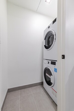 Ein Waschraum mit zwei übereinander gestapelten Waschmaschinen mit Frontlader, einem Fliesenboden und einer weißen Wand.