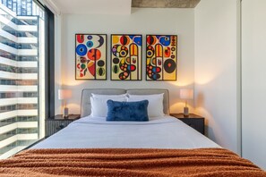 Ein Hotelzimmer mit einem großen Bett, zwei Nachttischen und abstrakter Kunst an der Wand.