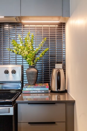 Uma cozinha com fogão moderno, chaleira, planta em vaso e uma pilha de livros de receitas.