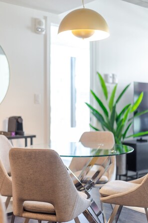 Uma sala de jantar moderna com mesa de vidro, cadeiras bege e luminária pendente.