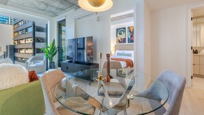 Un salon moderne avec une table à manger en verre, des sièges confortables, un téléviseur à écran plat et une grande fenêtre donnant sur un immeuble.