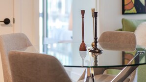 Un espace repas moderne avec une table en verre, deux chaises, une suspension et un tableau au mur.