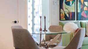 Un salon moderne avec une table basse en verre, deux fauteuils, un canapé vert et des tableaux abstraits accrochés au mur.