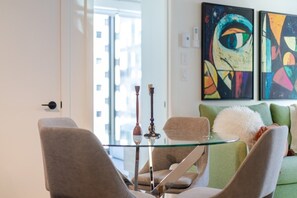 Ein modernes Wohnzimmer mit einem Glastisch, zwei Sessel, einem grünen Sofa und abstrakten Bildern an der Wand.