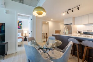 Una cocina moderna con una mesa de comedor de vidrio, taburetes de bar y una lámpara colgante.