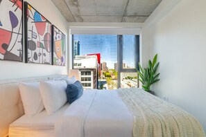 A modern bedroom with a large bed, a city view, and abstract art on the wall. - Chic Urban Retreat | Pool Gym & Terrace (Montreal)