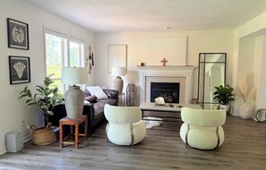 A living room with a fireplace, a sofa, two pouf chairs, a lamp, and framed artwork on the walls. - Serene 4-bedroom and 2.5 bathroom house charming Rockford (Rockford)