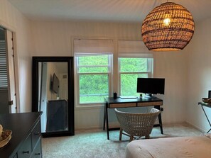Ein Schlafzimmer mit Bett, Schreibtisch mit Computer, Stuhl, Spiegel und zwei Fenstern.