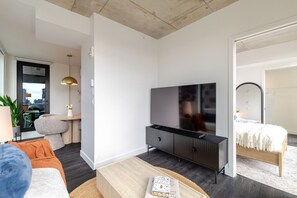 A modern living room with a flat-screen TV, a sofa, a coffee table, and a dining area with a small table and chairs. - Luxe Central Retreat | Free Parking & Pool (Montréal)