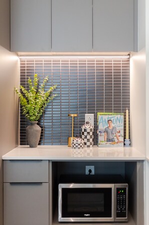 A kitchen area with a microwave, a potted plant, a magazine, and a candle on the counter. - Luxe Central Retreat | Free Parking & Pool (Montréal)