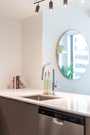 A modern kitchen with a stainless steel sink, a round mirror, and overhead lighting. - Luxe Central Retreat | Free Parking & Pool (Montréal)