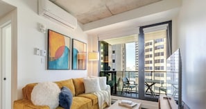 A modern living room with a sofa, a coffee table, and a large window with a view of buildings. - Luxury Stay | Free Parking (Montréal)