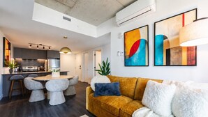 A modern living room with a sofa, a dining table with stools, and a kitchen area in the background. - Luxury Stay | Free Parking (Montréal)