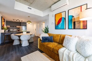 A modern living room with a sofa, a dining table with stools, and a kitchen area in the background. - Luxury Stay | Free Parking (Montréal)