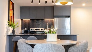 A modern kitchen with grey cabinets, a stainless steel refrigerator, and a round dining table with grey chairs. - Luxury Stay | Free Parking (Montréal)