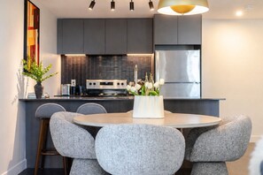 A modern kitchen with grey cabinets, a stainless steel refrigerator, and a round dining table with grey chairs. - Luxury Stay | Free Parking (Montréal)