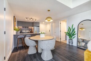 Een moderne keuken met grijze kastjes, een centraal eiland en een eetgedeelte met een ronde tafel en stoelen.