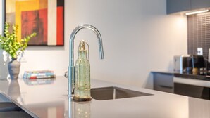 Cozinha moderna com torneira de aço inoxidável, garrafa de vidro e um vaso com plantas verdes.